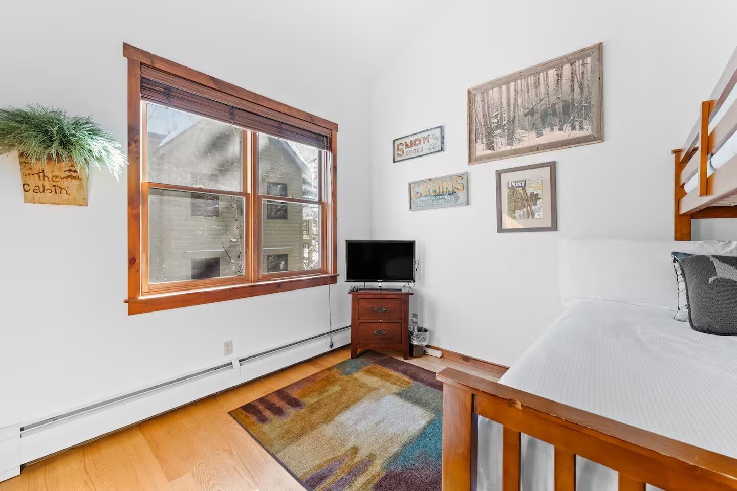 A bedroom with a large window, a TV, a dresser, a bed, and a rug.