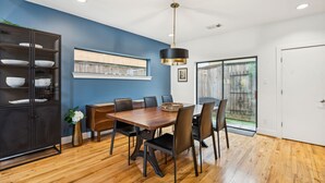 Un coin repas avec une table en bois, des chaises noires, un buffet sombre doté d’étagères et un ventilateur de plafond.