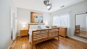 Une chambre à coucher avec un lit en bois, des tables de chevet, une commode, un miroir et un tableau accroché au mur.