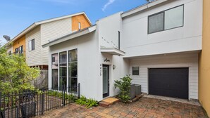 Un immeuble résidentiel moderne à deux étages, doté d’un garage, d’un petit jardin devant et d’un chemin d’accès en briques.