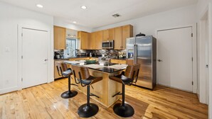 Une cuisine moderne dotée de meubles en bois, d’appareils électroménagers en acier inoxydable et d’un îlot central agrémenté de tabourets de bar.