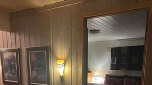 A cozy room with a leather sofa, a framed picture, a wall-mounted lamp, and a sliding door leading to a bedroom with a bed and a nightstand.