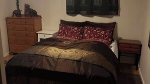 A bedroom with a bed, dresser, nightstand, and a wall-mounted tapestry.