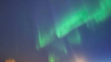 A night view of the Northern Lights over a town with visible buildings and a hill.