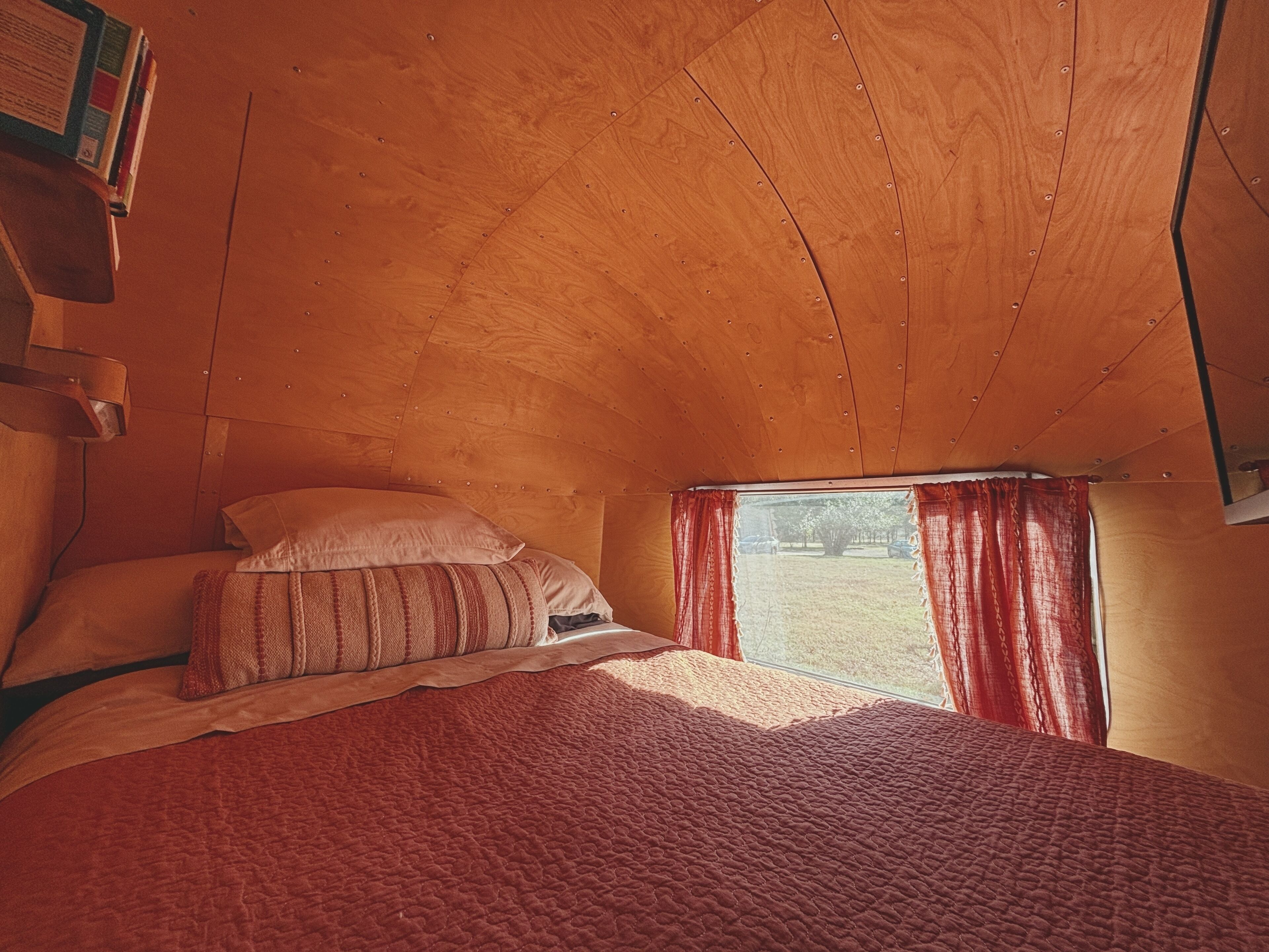 Un dormitorio con techo de madera, una cama con colcha roja y una ventana con cortinas rojas.