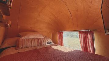 Un dormitorio con techo de madera, una cama con colcha roja y una ventana con cortinas rojas.