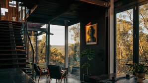 Un intérieur moderne avec un escalier, un coin salon et de grandes fenêtres offrant une vue sur les arbres et les collines.