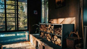 Une pièce dotée d’une grande fenêtre, d’une cheminée et d’une étagère où est entreposé du bois de chauffage.
