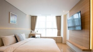 Una habitación de hotel con cama, escritorio, televisor montado en la pared y ventana con cortinas.