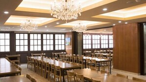 Un comedor amplio con varias mesas y sillas de madera, ventanas grandes y candelabros.