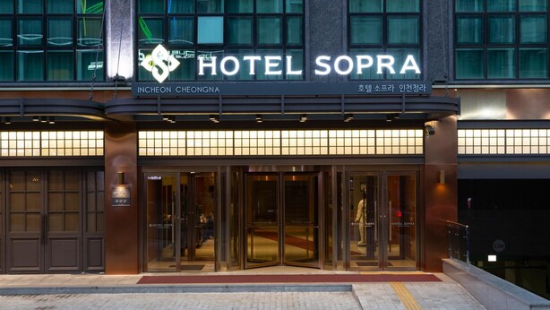La entrada del Hotel Sopra, con un diseño moderno, presenta grandes puertas de vidrio y una vista despejada al vestíbulo.