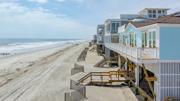 A beachfront property with multiple levels of wooden decks and railings, leading to a sandy beach and ocean view. - Oceanfront Family Retreat with Kids' Amenities & Stunning Views (Folly Beach)