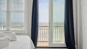A bedroom with a view of the ocean, a bed with white linens, and a door leading to a balcony. - Oceanfront Family Retreat with Kids' Amenities & Stunning Views (Folly Beach)