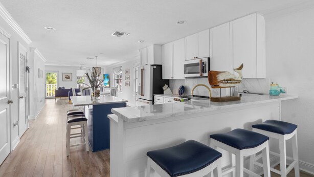 A modern kitchen with white cabinetry, a central island with bar stools, and a view into the adjacent living area. - Stylish 3-Story Home w/ Heated Pool & Palm Views (Naples)