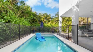 A swimming pool with a blue chair, surrounded by a fence and greenery. - Stylish 3-Story Home w/ Heated Pool & Palm Views (Naples)