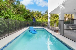 A swimming pool with a blue chair, surrounded by a fence and greenery.