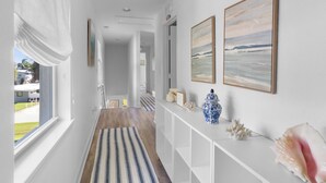 A hallway with a striped rug, white console table with decorative items, and framed artwork on the walls. - Stylish 3-Story Home w/ Heated Pool & Palm Views (Naples)
