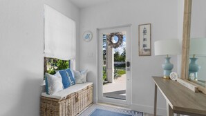 A clean, modern entryway with a wicker bench, a blue rug, a wooden console table, and a mirror. - Stylish 3-Story Home w/ Heated Pool & Palm Views (Naples)
