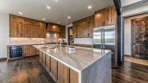 A modern kitchen with wooden cabinets, a marble island, stainless steel appliances, and a built-in dishwasher.