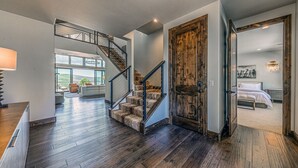 A spacious living area with a staircase leading to a loft, a large wooden door, and a bedroom with a bed and nightstand.