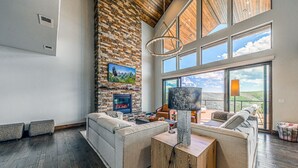 A modern living room with a fireplace, large windows, and a high ceiling.