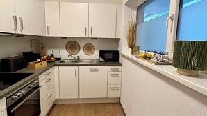 A modern kitchen with white cabinets, a black stove, and a window with a view of the sky.