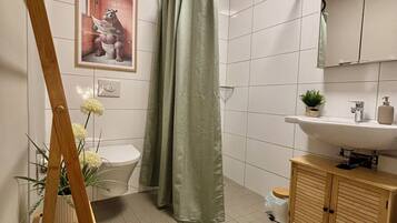 A bathroom with a toilet, a sink, a mirror, a shower curtain, and a wooden bench.