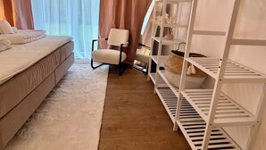 A bedroom with a bed, a chair, a white shelving unit, and a large window with curtains.