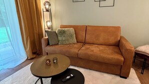 A living room with a brown sofa, a white rug, two round tables, and two wall-mounted plants.