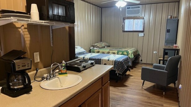 Une petite pièce comprenant un coin cuisine, un lit, une chaise et un ventilateur de plafond.