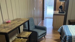 Une pièce de taille modeste avec un plancher en bois, un lit recouvert d’une courtepointe à motifs, un petit bureau avec une chaise et un téléviseur posé sur un meuble.