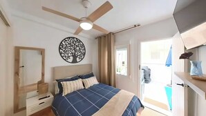 A bedroom with a bed, a ceiling fan, a wall-mounted tree decoration, a bedside table, and a window with curtains. - Tranquil 2-bedroom apartment with AC in La Mata (La Mata)