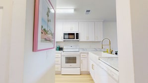 Una cocina con armarios blancos, microondas, estufa y un lavabo con grifo dorado.