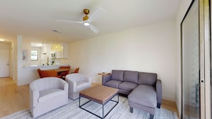Una sala de estar moderna con un sofá gris, dos sillones, una mesa de centro y un ventilador de techo.