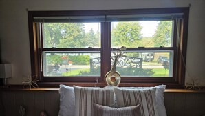 A bedroom with a large window, a bed with striped and solid pillows, a bedside table with a lamp, and a decorative metal piece on the window sill. - Hot Tub Retreats (Lake Villa)