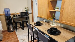 A compact kitchen with a wooden table, black plates, a water dispenser, a microwave, and a small plant on the counter. - Hot Tub Retreats (Lake Villa)