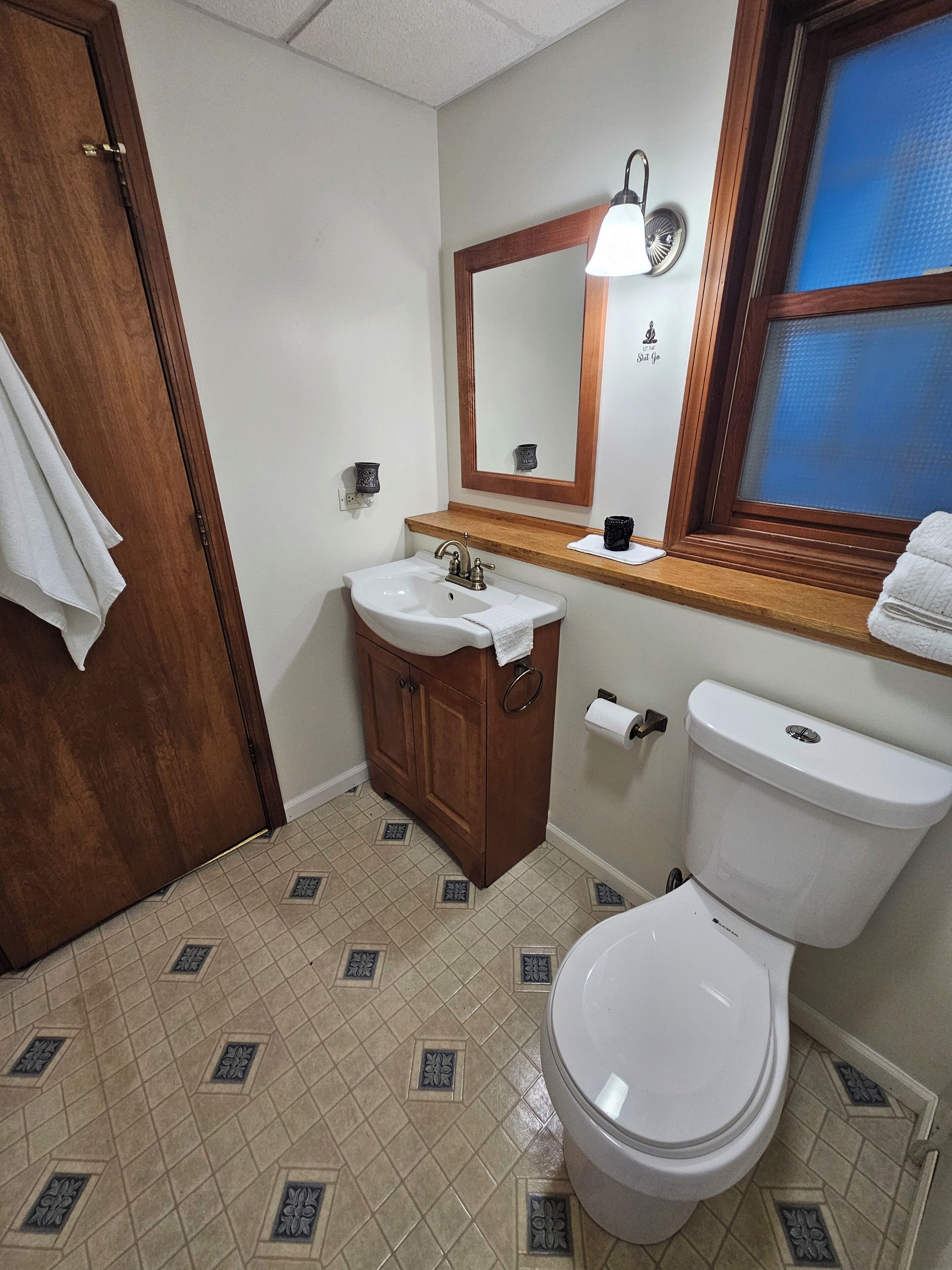 Ein Badezimmer mit Holztür, Waschbecken mit Handtuch, Toilette und Fenster mit Blick.