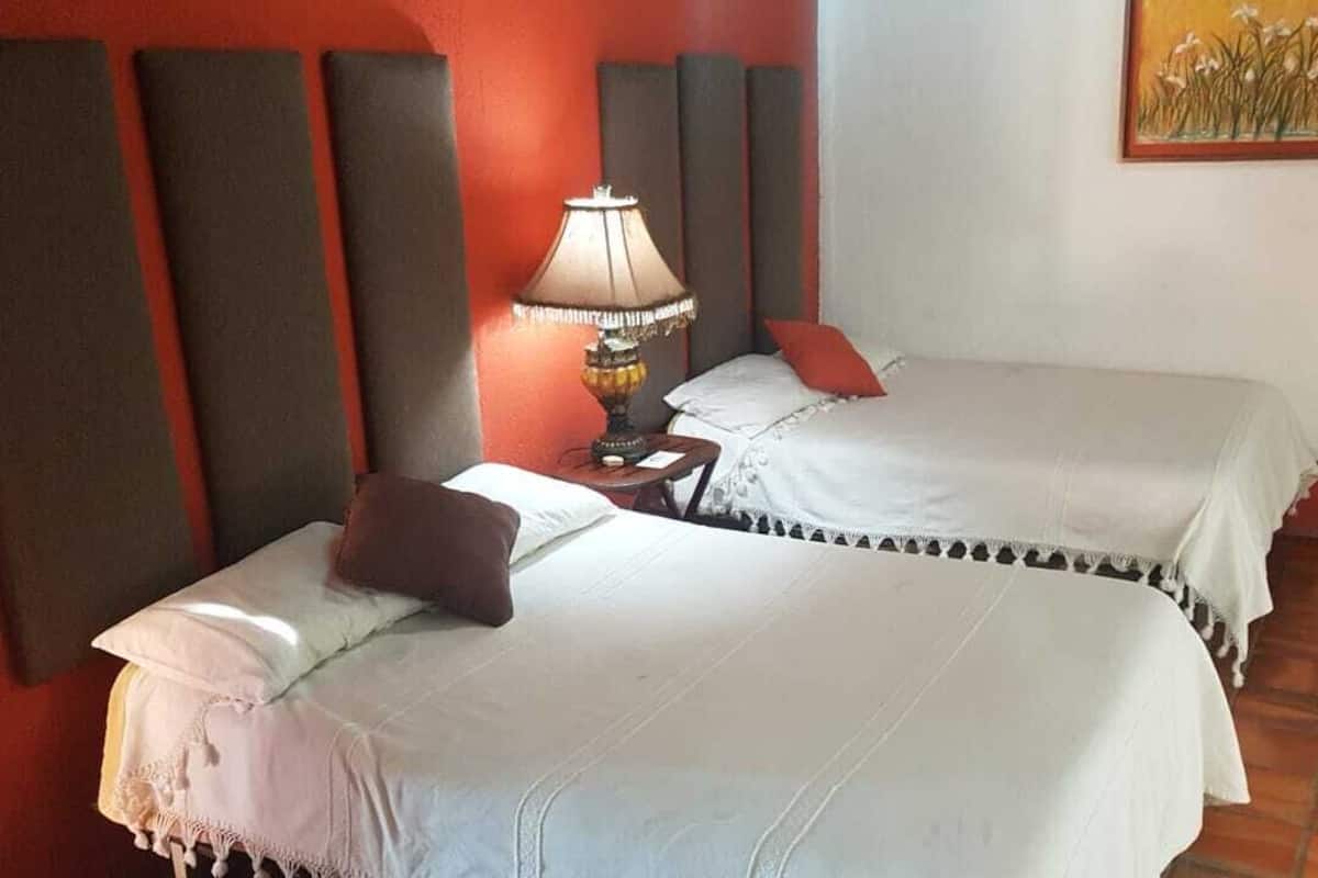 Habitación de hotel con dos camas, una mesita de noche con lámpara y un cuadro en la pared.