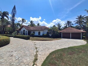 A house with a stone pathway leading to a garage, surrounded by palm trees and a clear sky. - Villa in Sea Horse Ranch, Cabarete's Most Exclusive Oceanfront Gated Community! (Sosúa)