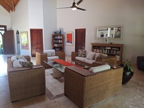 A spacious living room with wicker furniture, a glass coffee table, and a bookshelf.