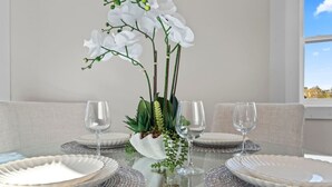 Une table à manger dressée avec de l’argenterie blanche, deux verres à vin et un centre de table composé d’orchidées blanches et de feuillage vert.