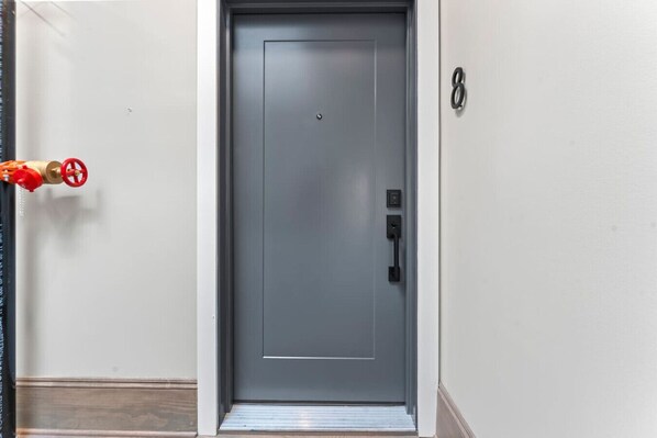 A grey door with a handle and a keyhole, a red fire alarm, and a number '8' on the wall.