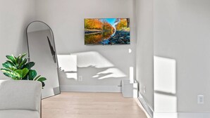 Une pièce au décor minimaliste, avec une grande fenêtre, un tableau représentant un paysage, une plante et un lampadaire au design moderne.