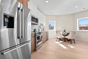 A modern kitchen with stainless steel appliances, wooden cabinets, and a dining area with a table and chairs.