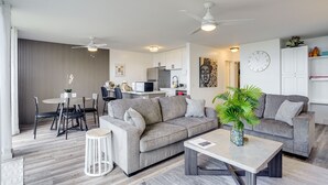 Un salón moderno con un sofá gris, una mesa de comedor y una cocina al fondo.