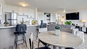 Una cocina moderna con armarios blancos, un refrigerador de acero inoxidable y una zona de comedor con una mesa redonda y sillas.