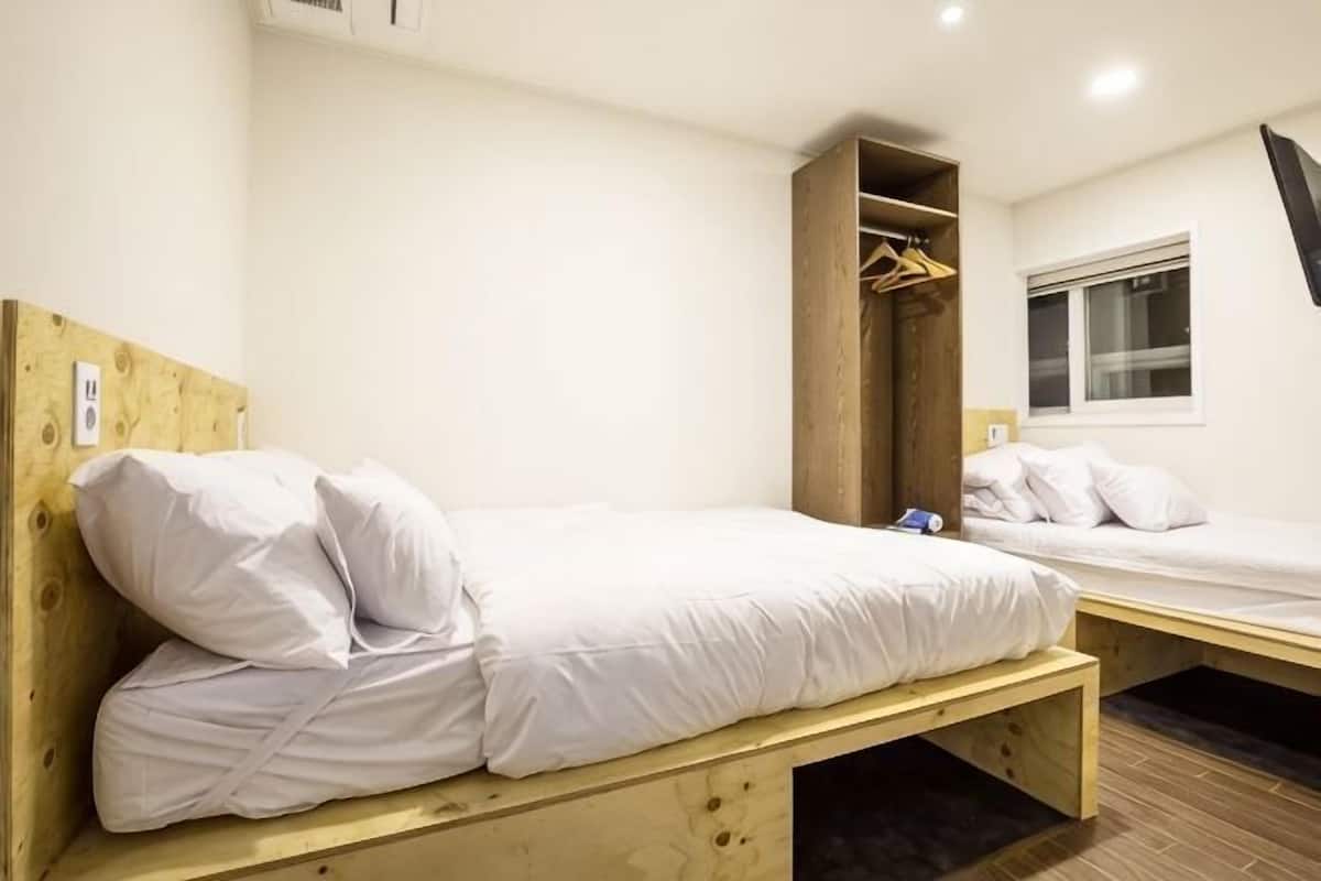 A room with two beds, wooden headboards, a wardrobe, and a window.