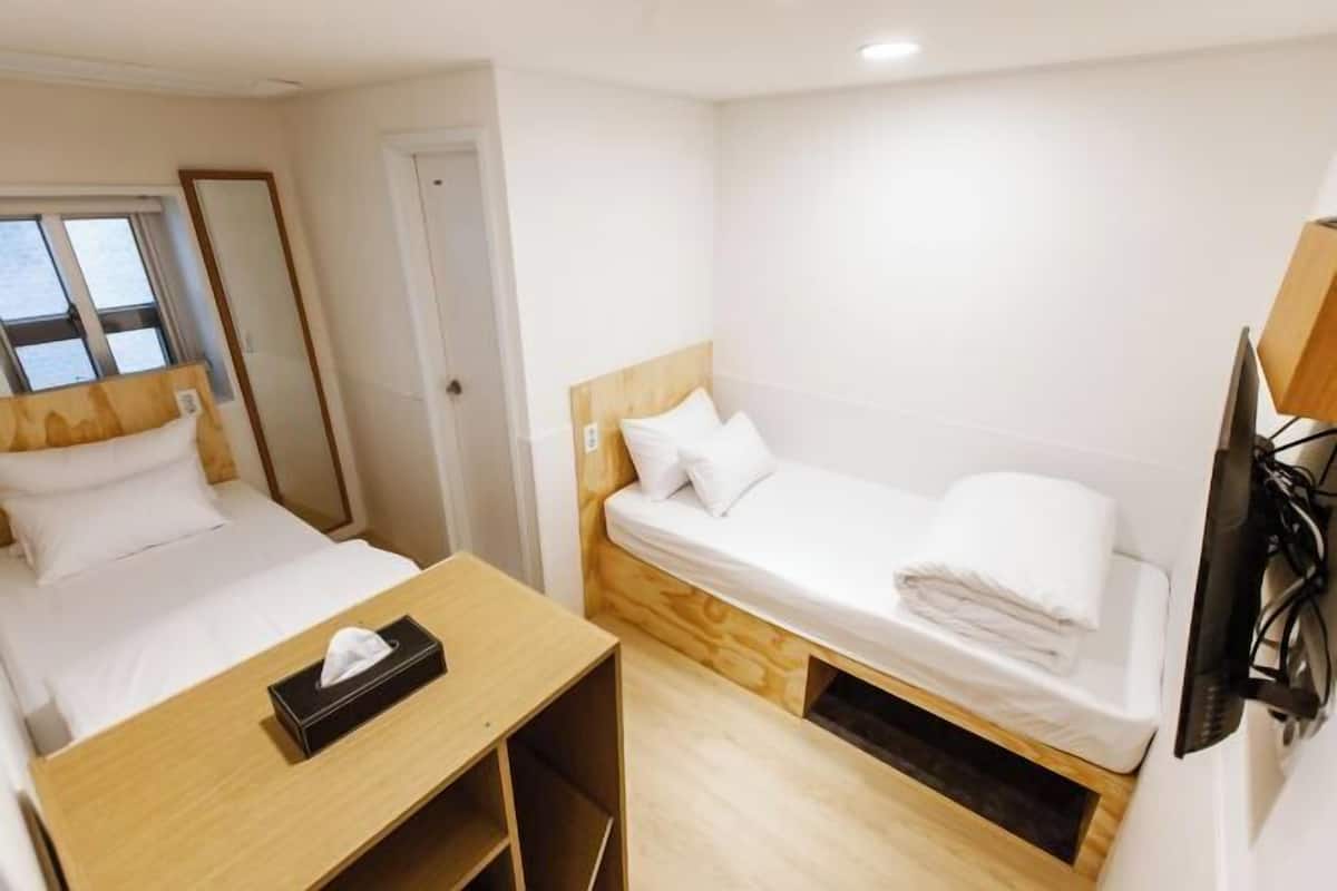 Habitació d'hotel compacta amb un llit individual, un escriptori petit i una televisió.