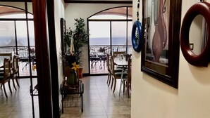 Amplia habitación con un gran ventanal que ofrece vistas al mar, un comedor con sillas y una mesa, y una obra de arte enmarcada en la pared.