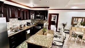 Una cocina moderna con armarios oscuros, encimeras de granito y una isla central con taburetes de bar.